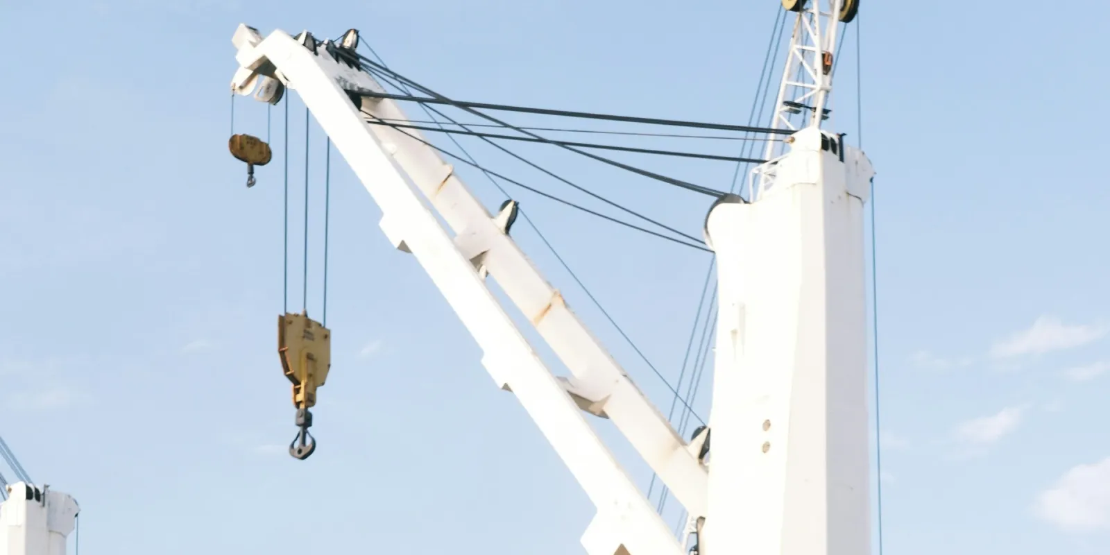 A white hydraulic deck crane on a cargo ship, its hook hanging from the jib