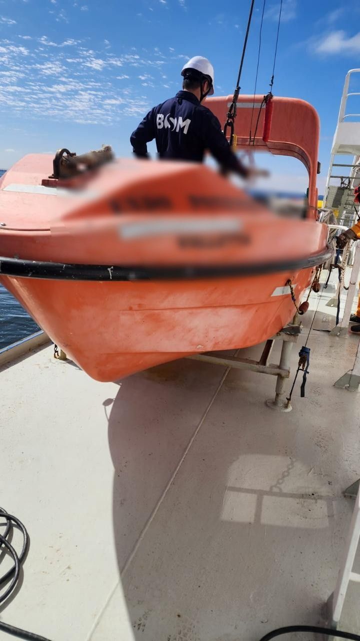 A technician working in an orange lifeboat on deck